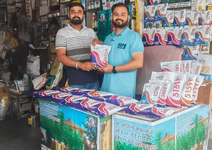 Two men holding a Neev Seeds packet at a seed shop counter